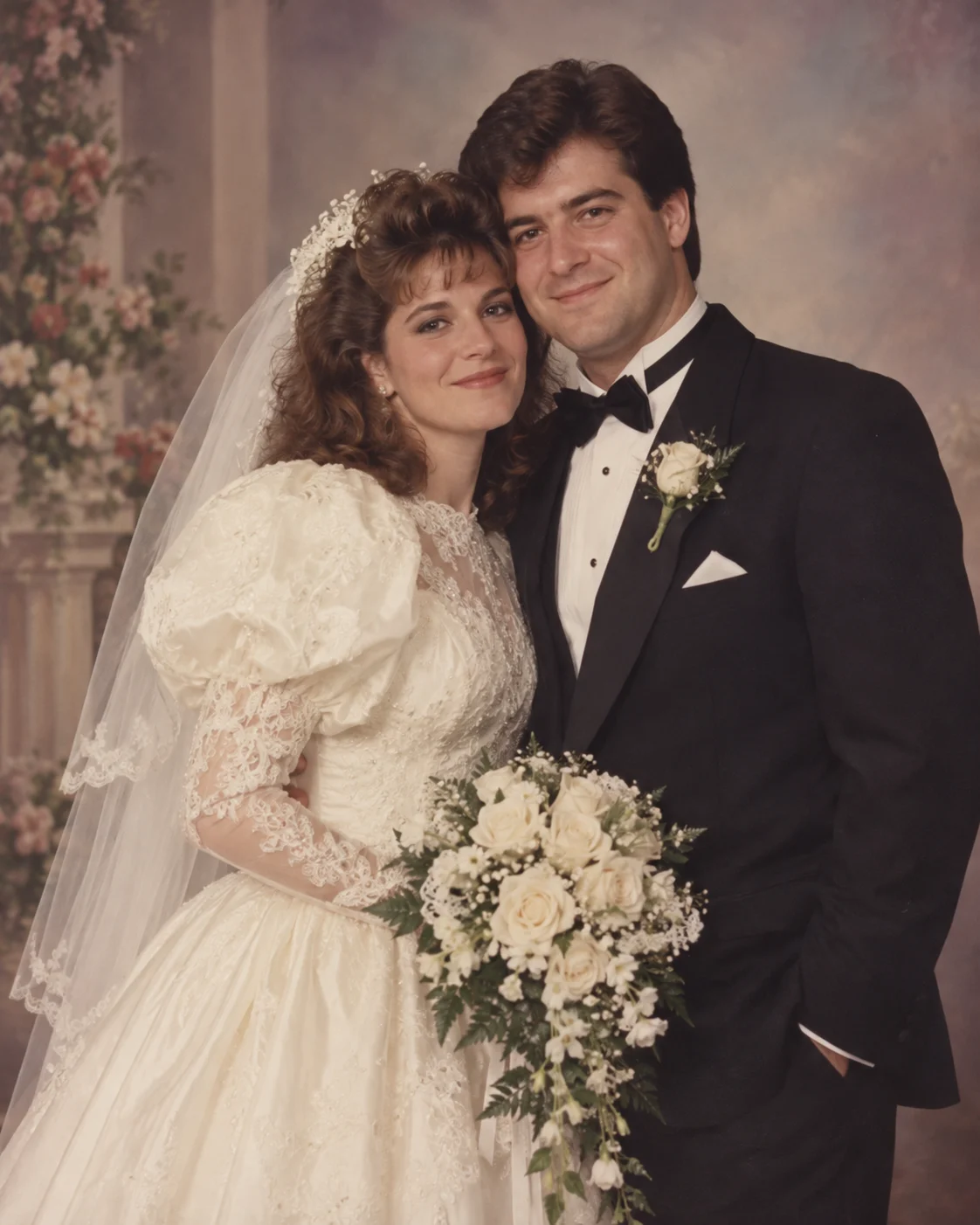 Bride in a puff-sleeve ivory gown beside a groom in a black tuxedo in a vintage studio wedding portrait