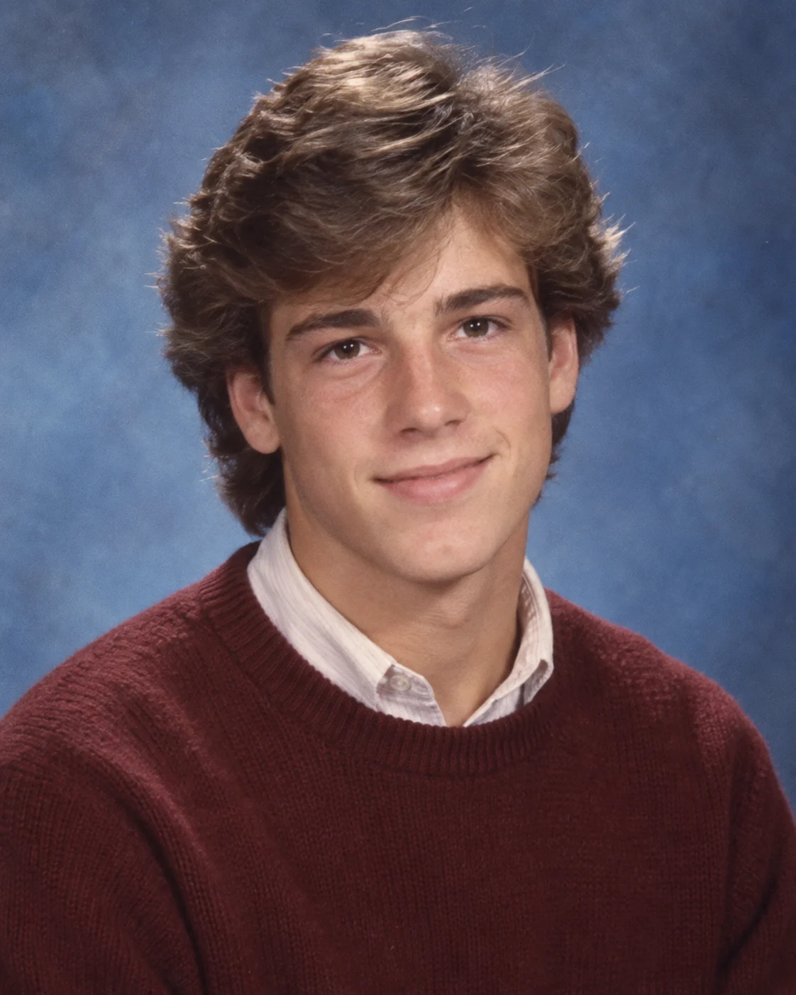 Student with feathered hair and a burgundy sweater posing against a mottled blue yearbook backdrop