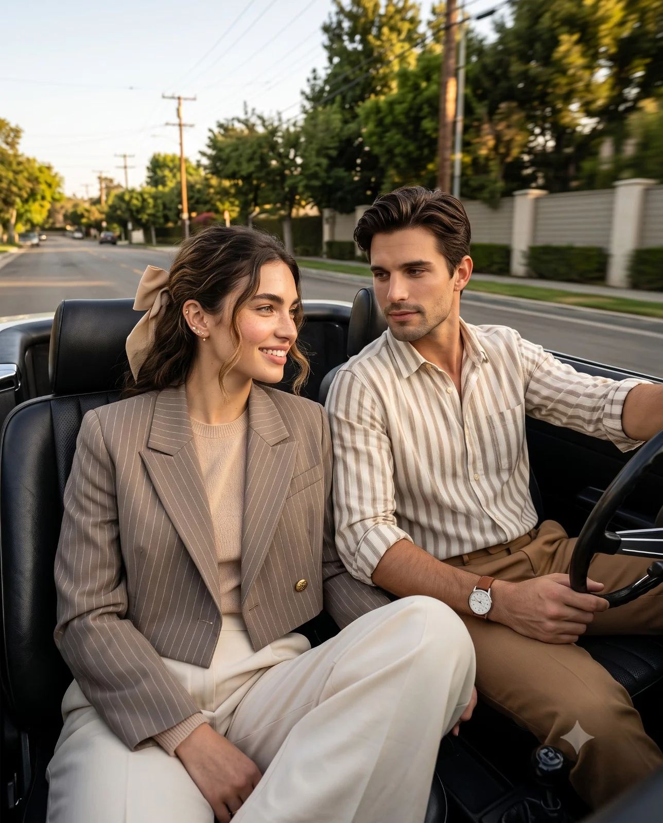 Stylish couple smiling at each other while driving an open-top convertible at golden hour