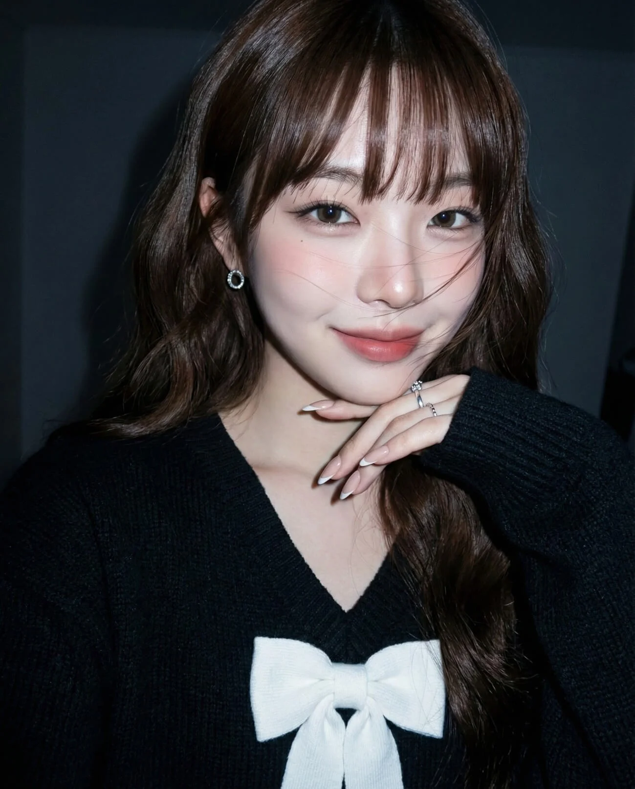 Woman with wavy brown hair and bangs posing in a black sweater under direct camera flash