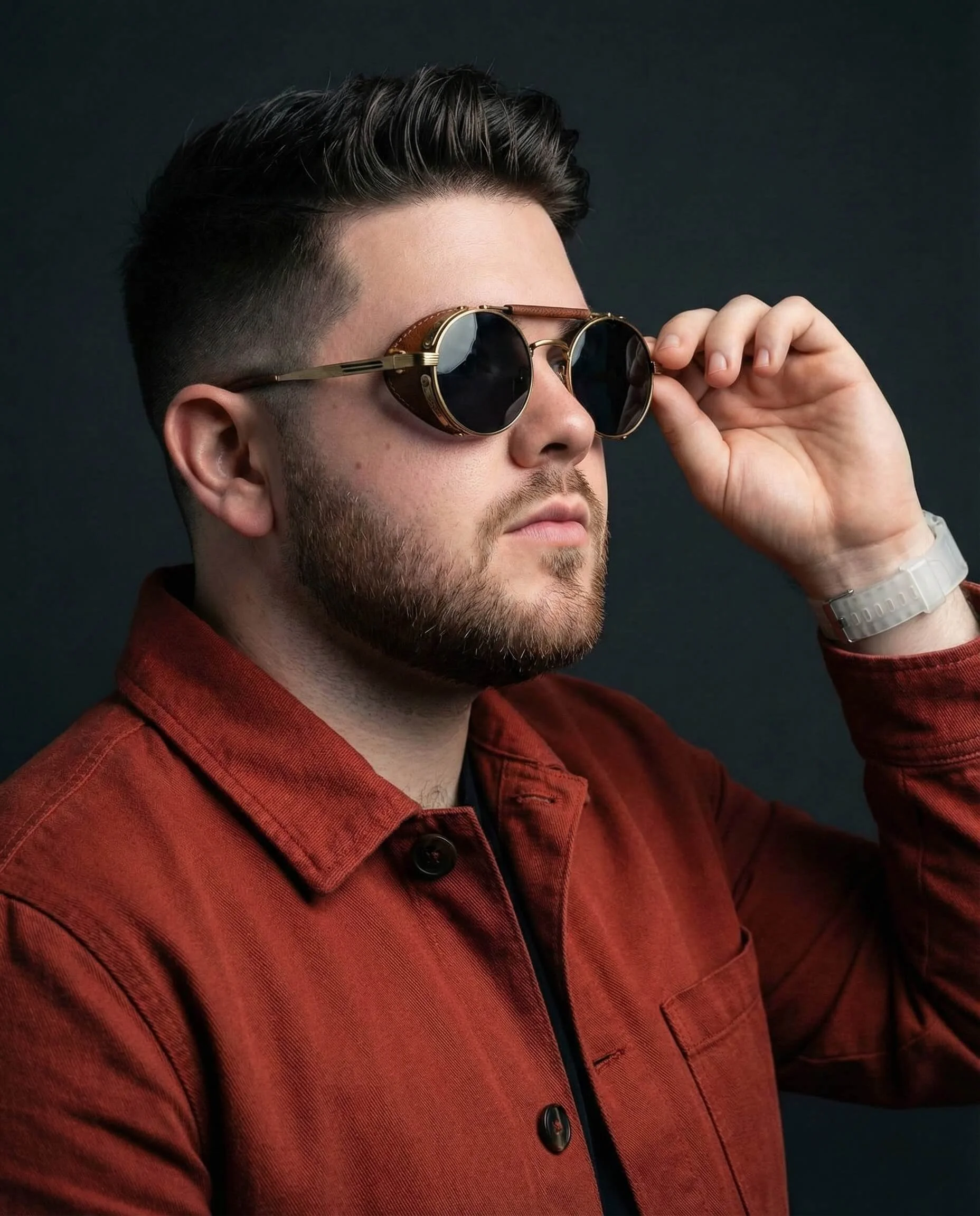 Man in a terracotta jacket adjusting round metallic steampunk sunglasses